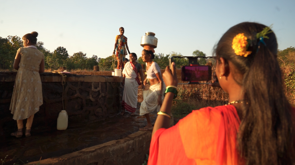 Three women in Khuded village, India fetching water from a well while a fourth woman films them.