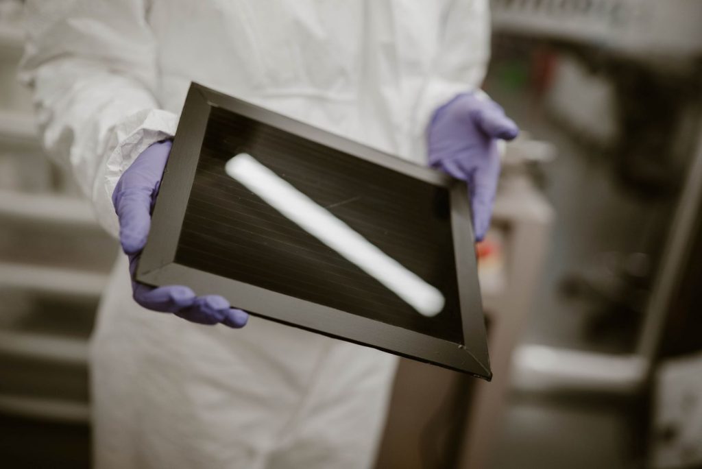 A person wearing protective lab gear holding an A4 perovskite solar module.